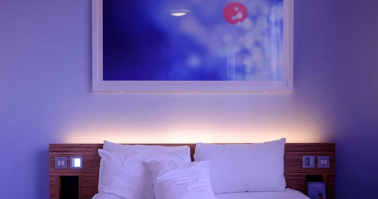 Cama de hotel com travesseiros empilhados na cabeceira e iluminação azul suave