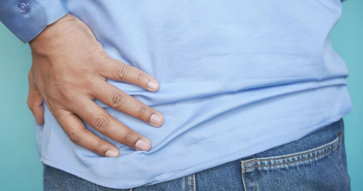 Pessoa de camisa azul e jeans com a mão apertando a lateral do quadril